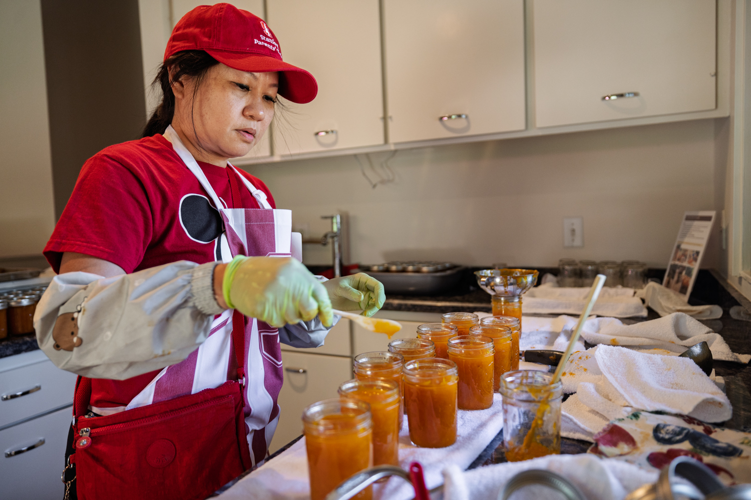 Woman in cap and apron filling glass jars with homemade apricot jam.