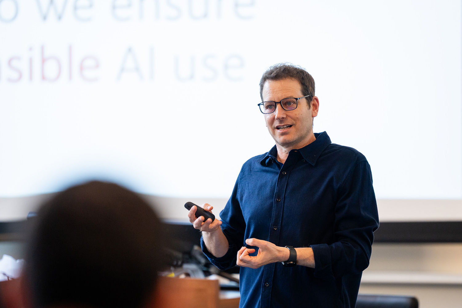 Amir Goldberg holds a clicker and gestures while speaking to a class, with a slide on responsible AI use behind him.