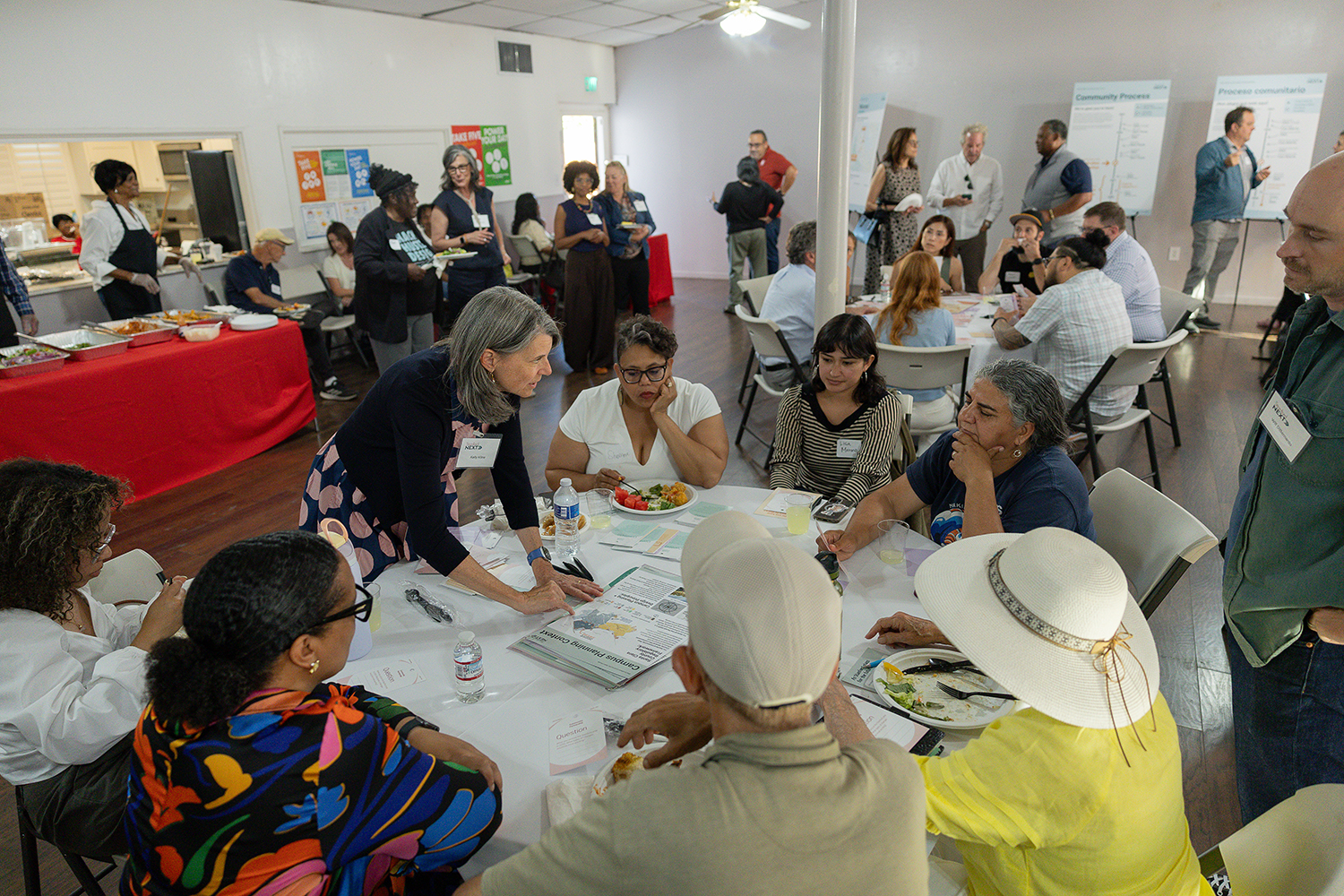 Community members gather over a meal to discuss campus planning, with informational posters displayed nearby.