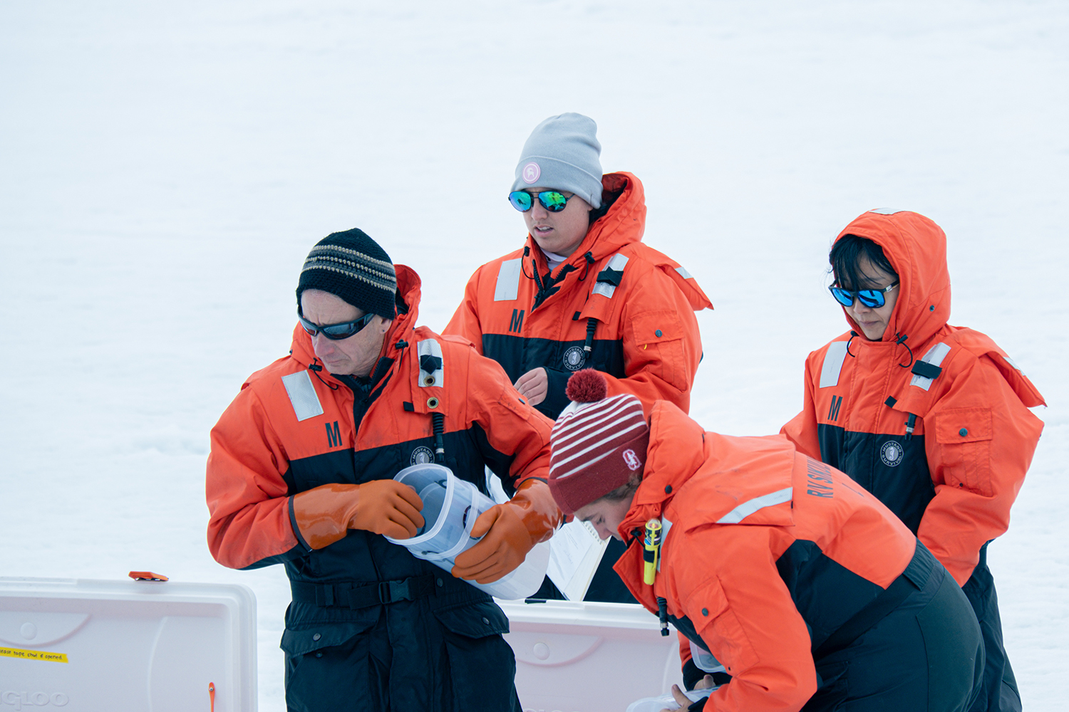 Four researchers in orange survival suits examine samples collected from the Arctic ice.