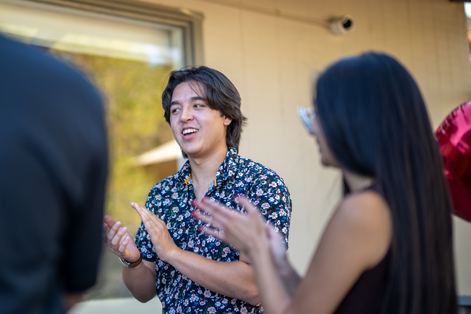 A student claps while chatting with friends outside a campus building.