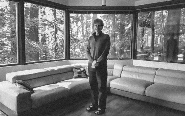Chris Chafe standing in a room surrounded by windows with views of redwood trees
