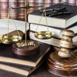 Wood gavel, bunch of keys, scales and stack of old books against the background of a row of antique books bound in leather