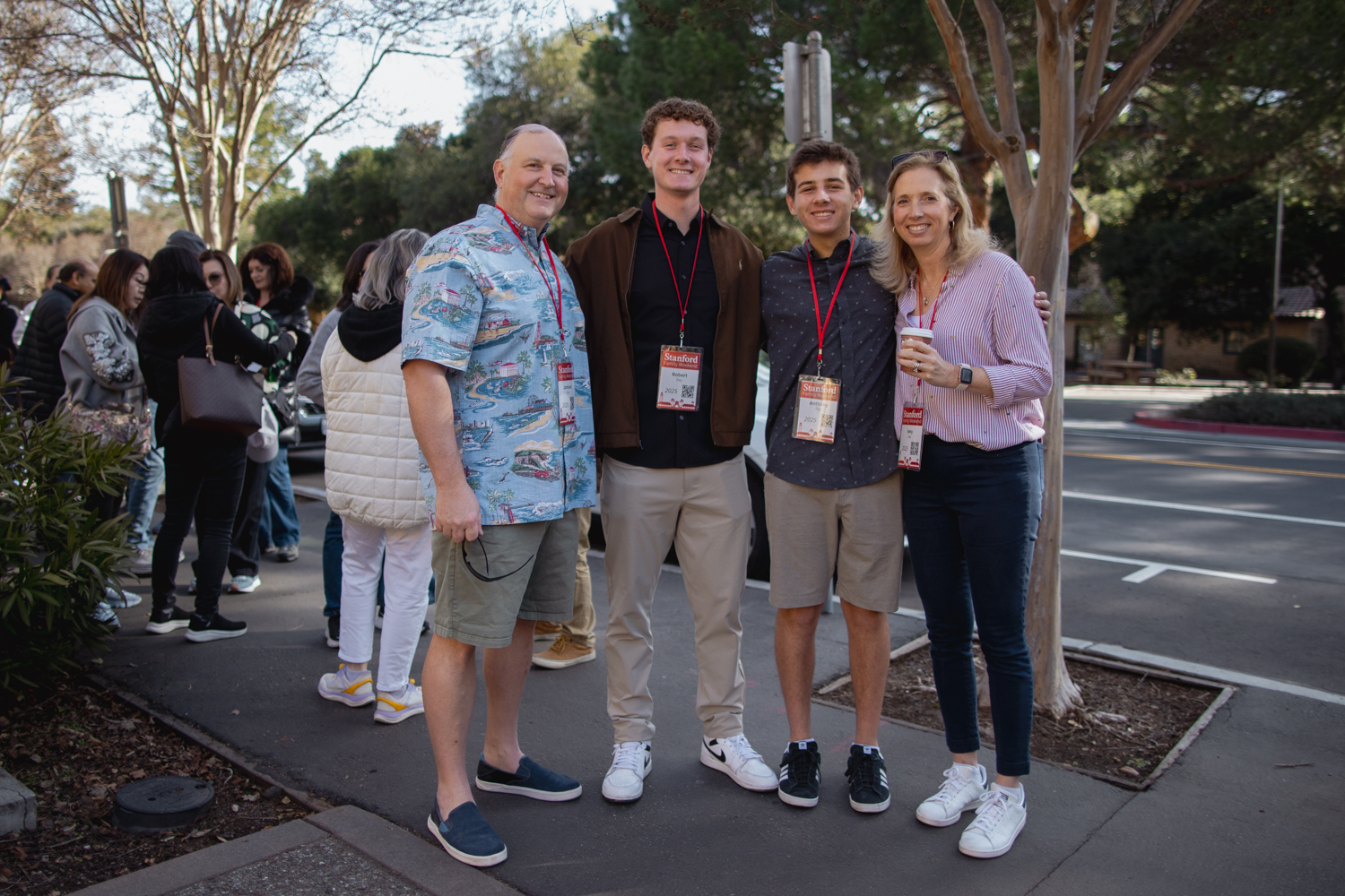 Family poses for a photo. Other families are gathered on the sidewalk in the background.