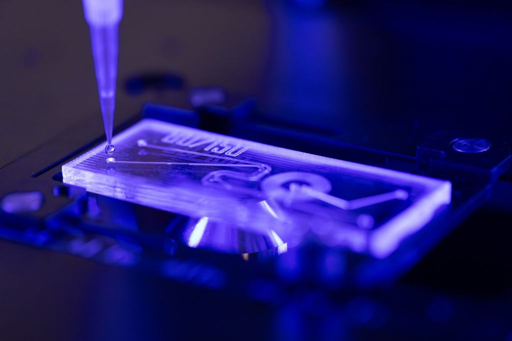 A close-up of a pipette dropping liquid onto a microfluidic device, designed for capturing images of genetically modified cells.
