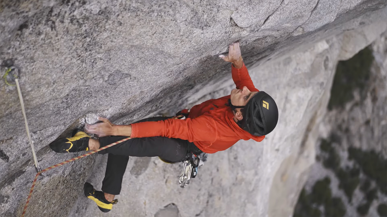 Connor Herson navigates a steep rock face, gripping the surface while secured with a rope.