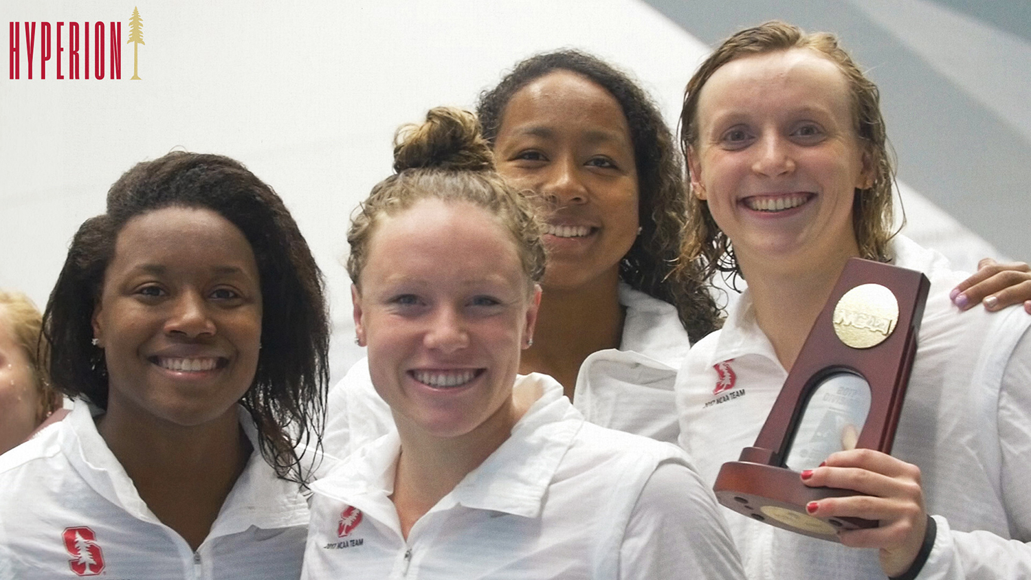 Swimmers celebrate their victory, posing together with a trophy, wearing matching team jackets after a championship event.