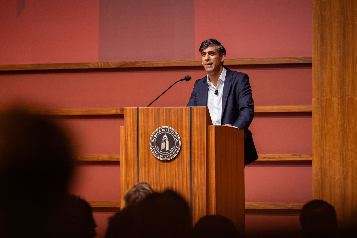 Rishi Sunak standing behind a podium, speaking into a microphone during an event at the Hoover Institution.