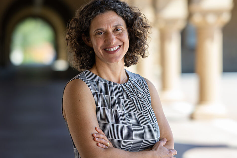 Dafna Zur smiling with curly hair and arms crossed wearing a patterned sleeveless top stands in Quad arcade.