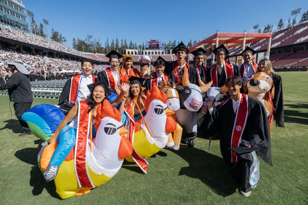 Open video Graduates pose with inflatable animal costumes, celebrating at a graduation ceremony on a sunny day in a stadium. in a modal