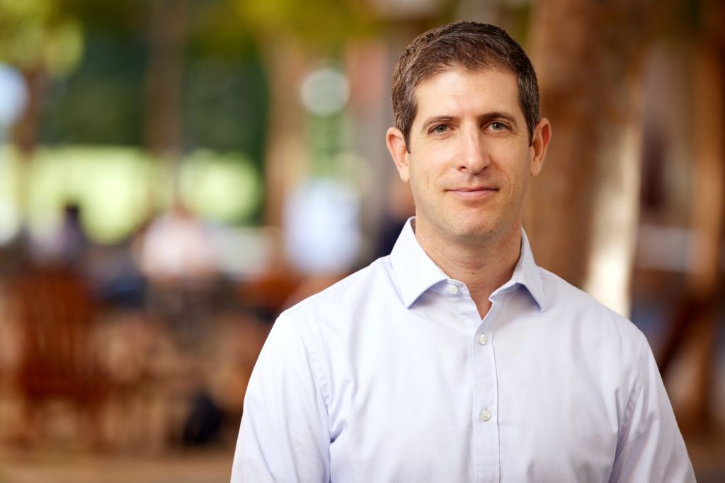Nir Halevy poses for a portrait outdoors with a blurred courtyard behind him.