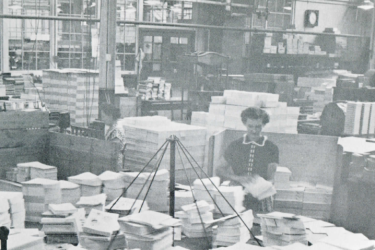 A 1959 photo shows a Stanford University Press worker at a folding table inside the press' facility.