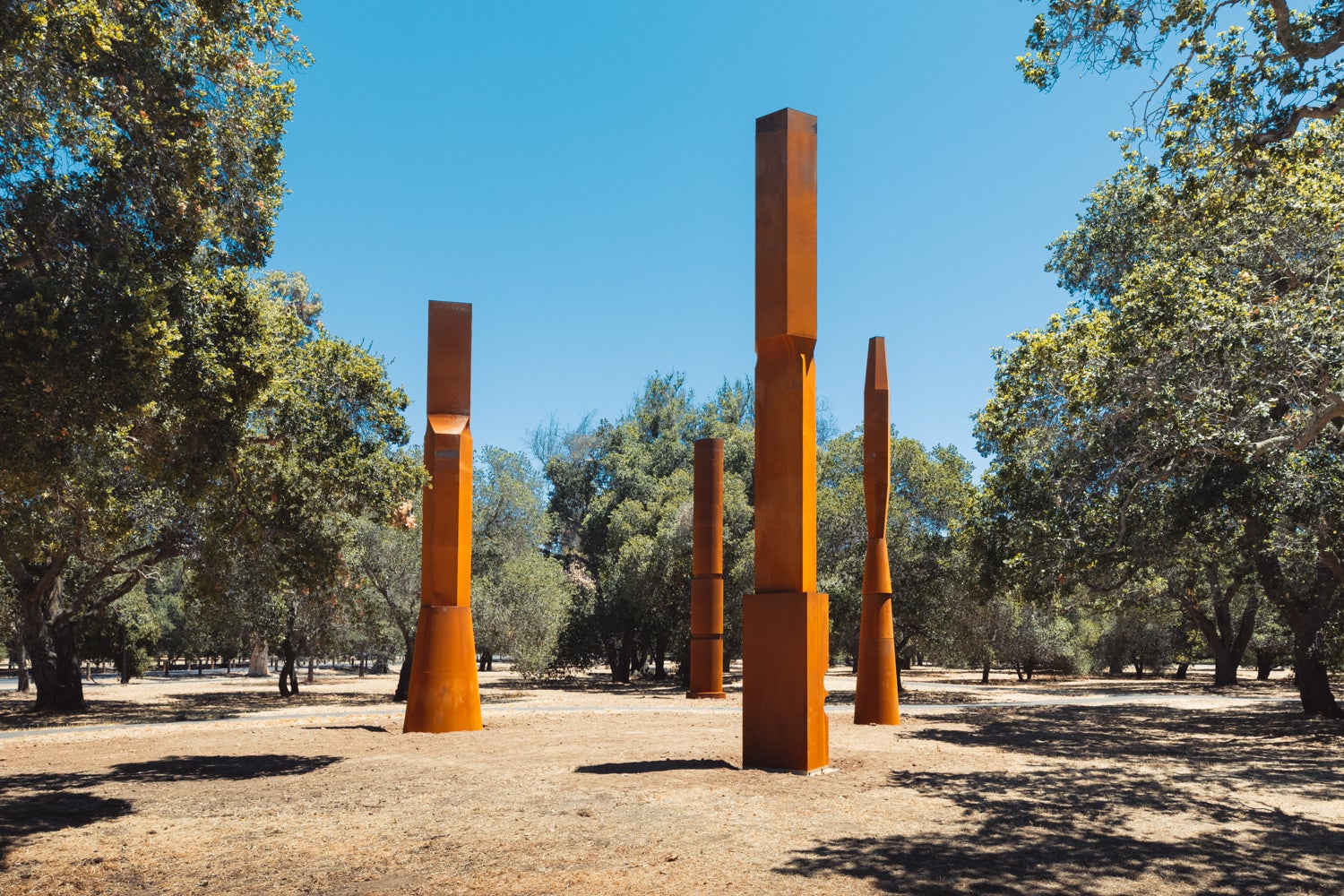 Four reddish-brown Cor-Ten steel tapered columns arranged in a square pattern in the Stanford Arboretum.