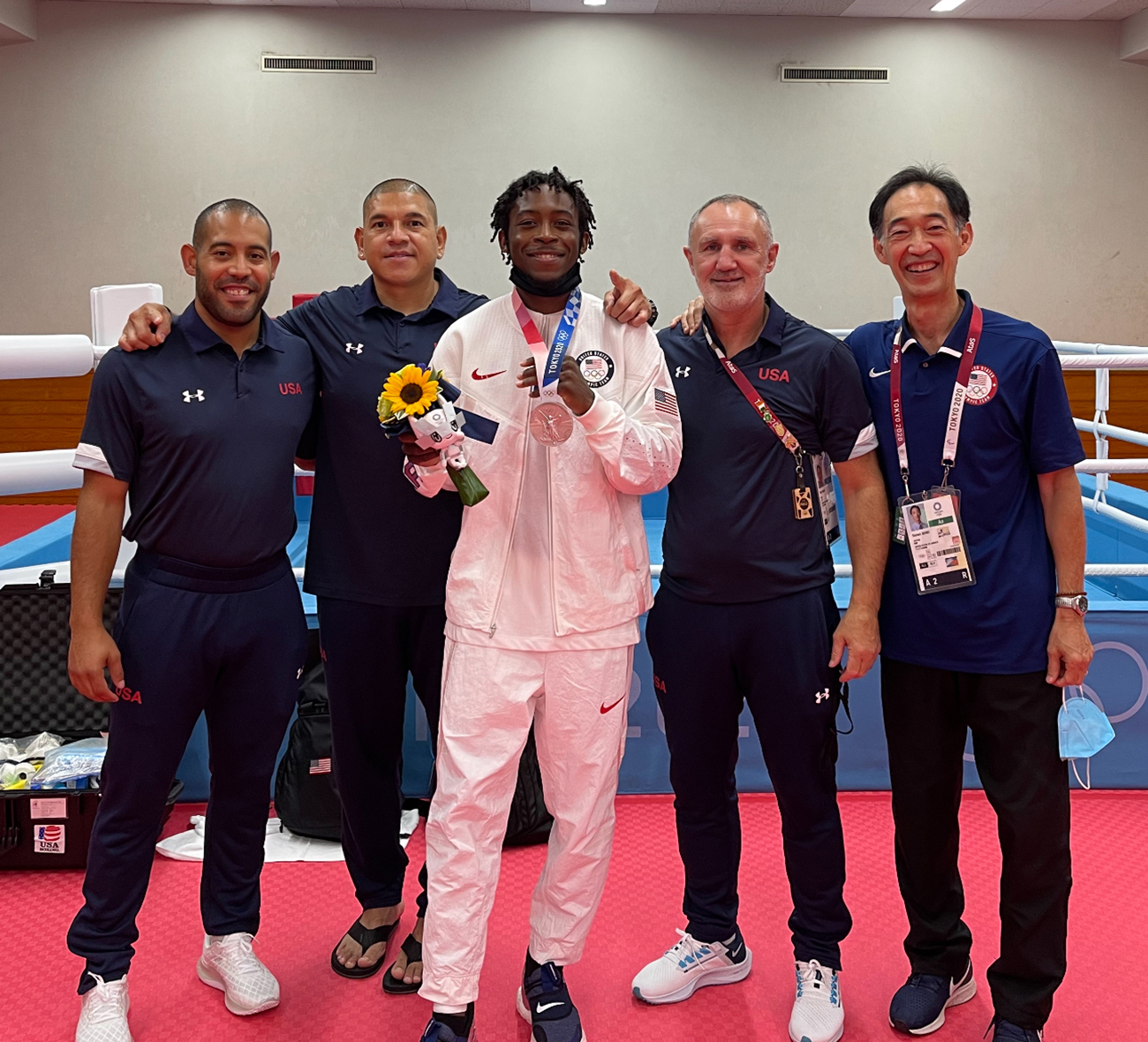 Dr. Steven Isono is pictured standing in front of a boxing ring with Olympian Keyshawn Davis, along with Dawson's trainer and head and assistant coaches.