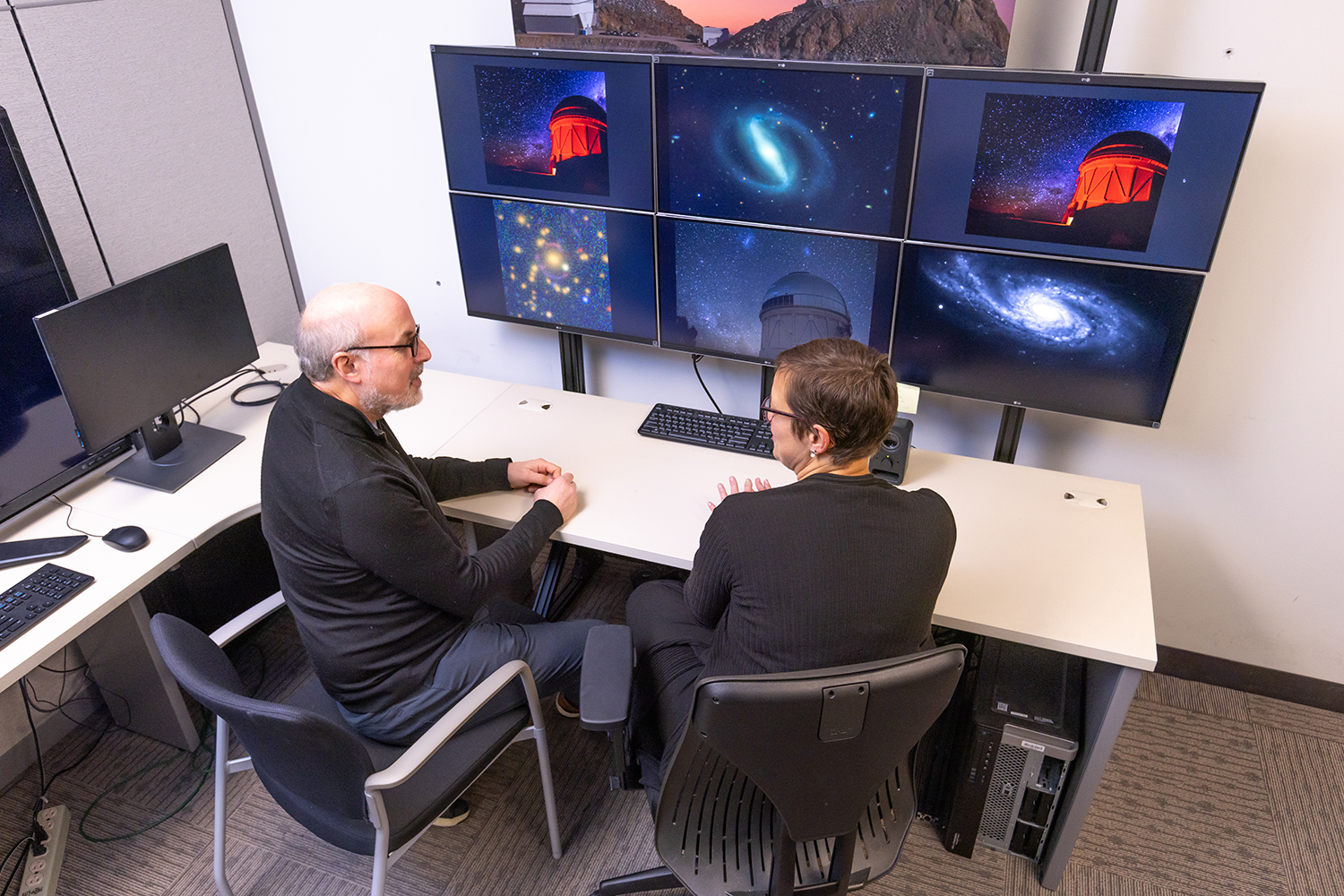 Josh Frieman and Risa Wechsler sit at a desk facing an array of monitors in the Rubin Control Room at SLAC.