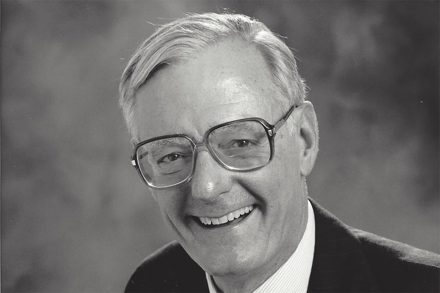 A black-and-white portrait of Buzz McCoy, with short hair and glasses, wearing a suit and tie.