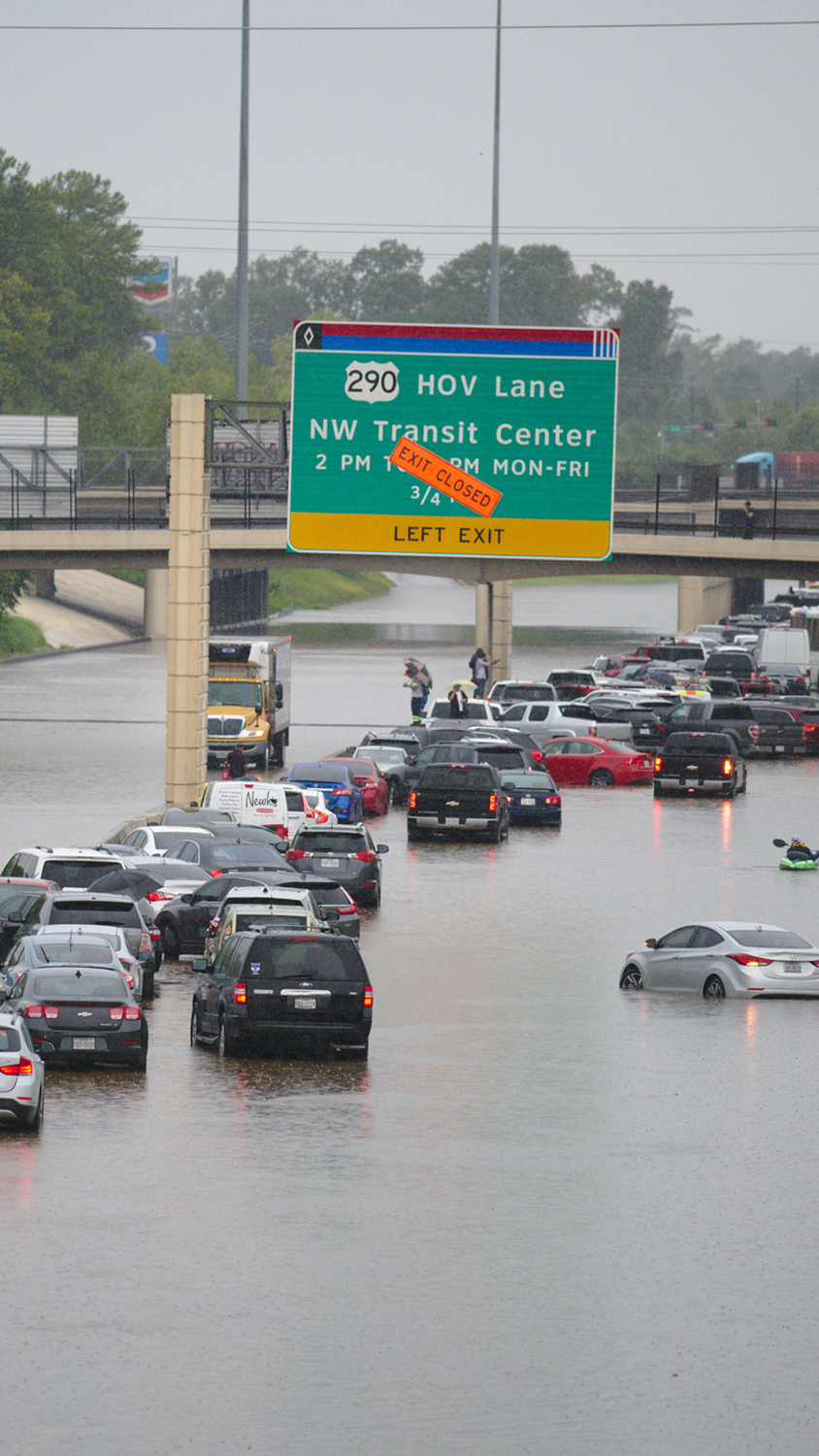 Heavy flooding causes traffic jams on a highway in Houston, Texas, with vehicles partially submerged and a road sign indicating closures.