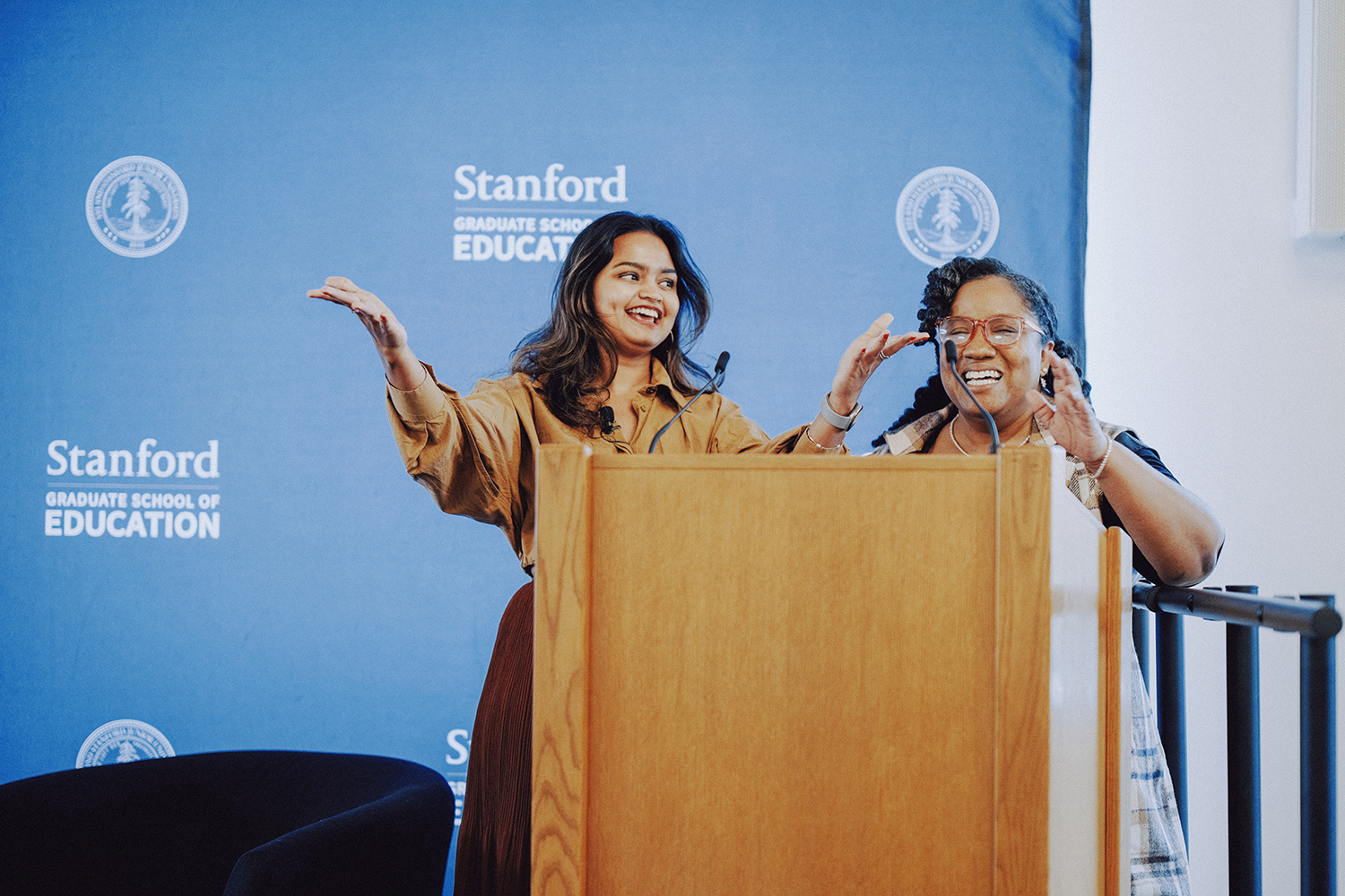 Two speakers engage with the audience from behind a podium at an event.