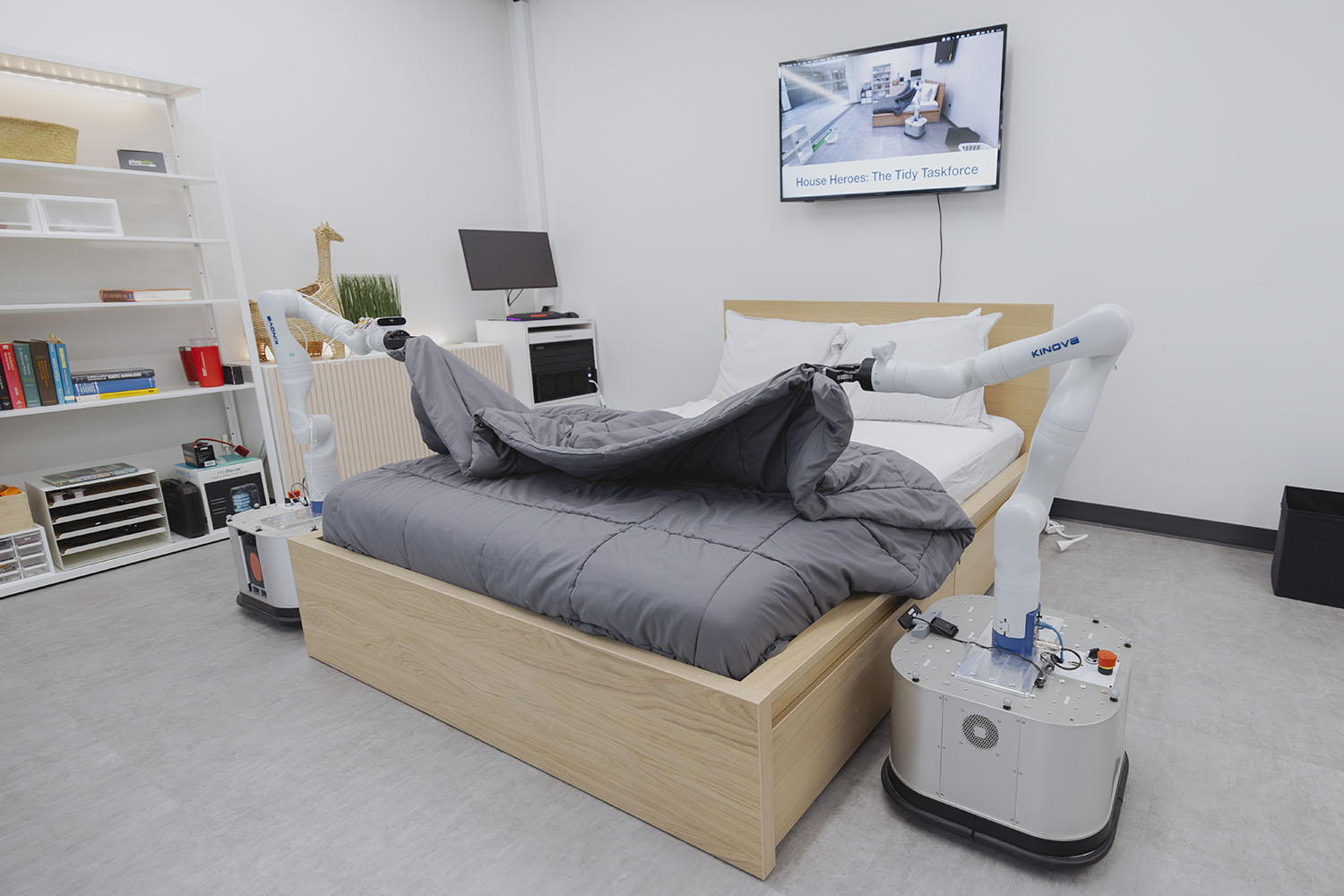 Robotic arms are tucking a blanket onto a bed in a modern bedroom setting.