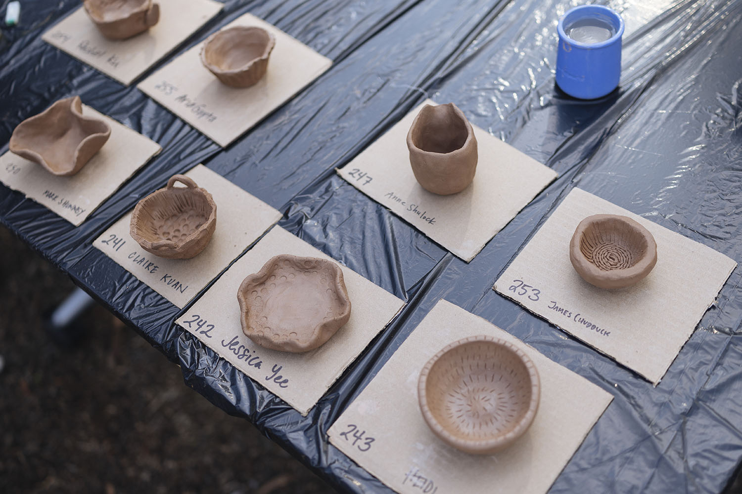 Clay bowls with different patterns sit on labeled cards at a pottery workshop table.