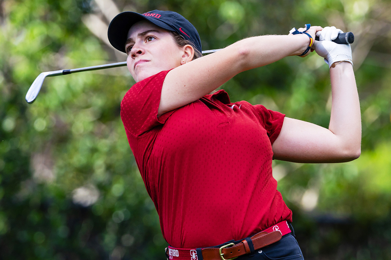 Paula Martin Sampedro swings a club on the course, wearing a red polo and black pants, with greenery in the background.