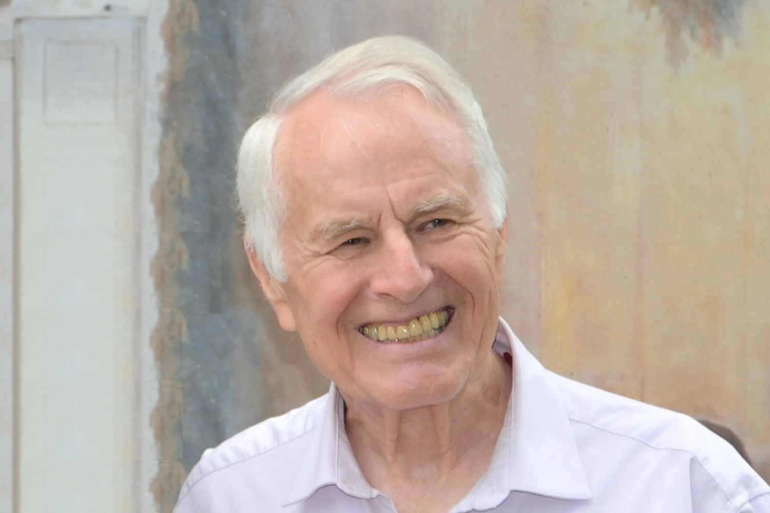 Portrait of Dagfinn Føllesdal wearing a collared shirt and standing against a soft, pastel-colored background.