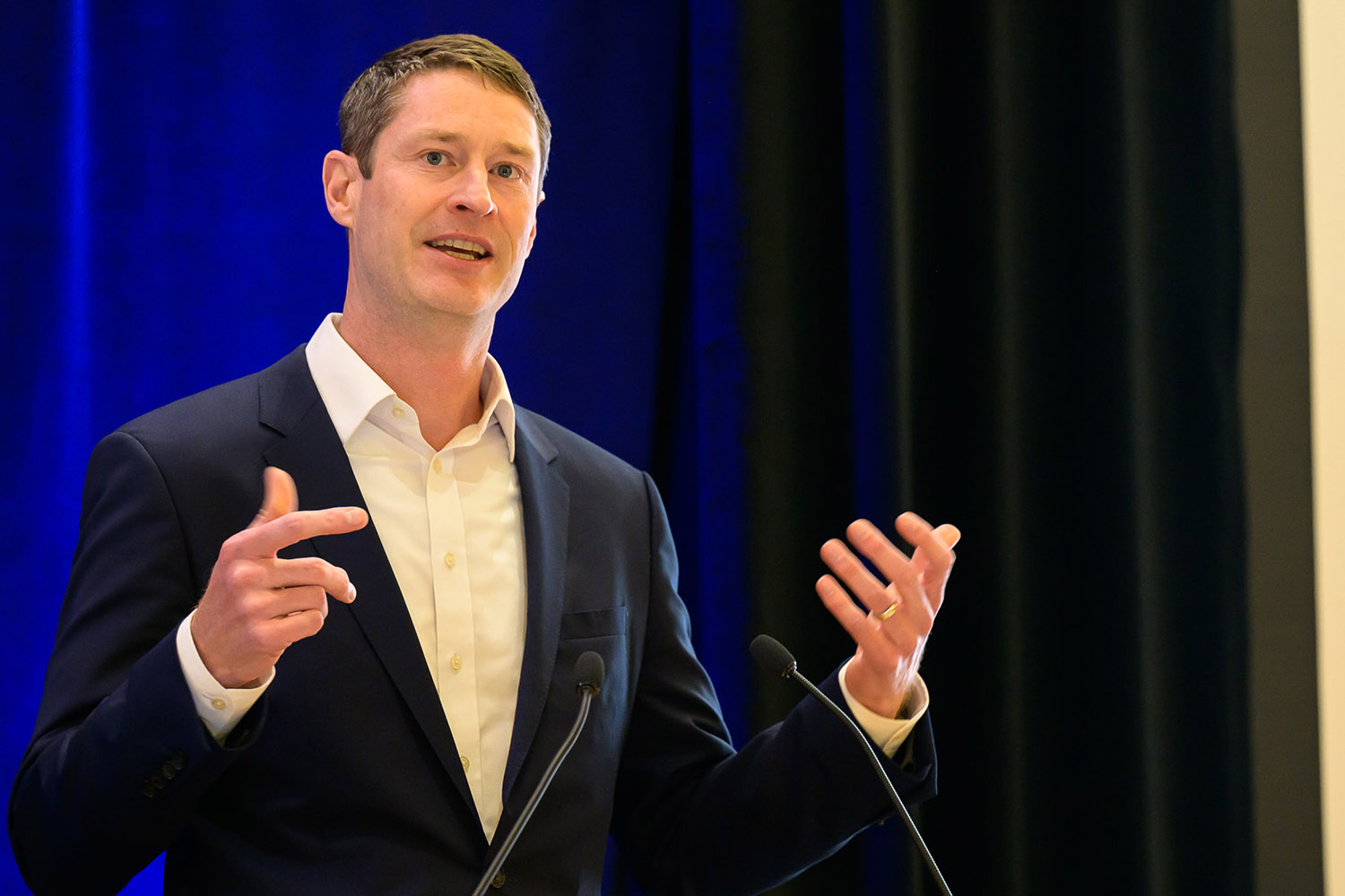 Jack Baker in a suit gestures while presenting at a lectern.