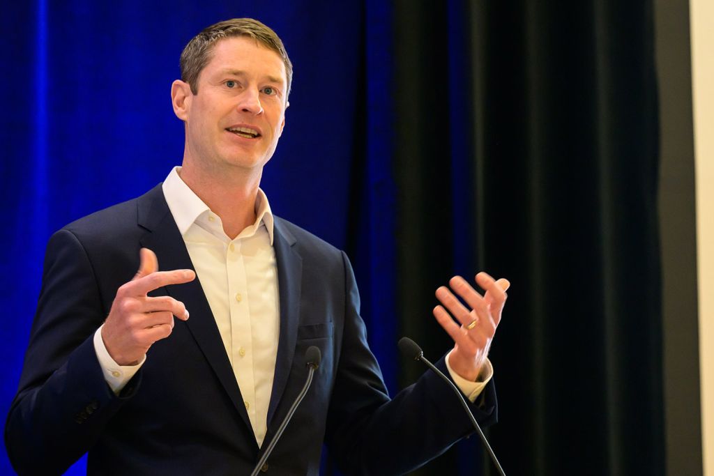 Jack Baker in a suit gestures while presenting at a lectern.