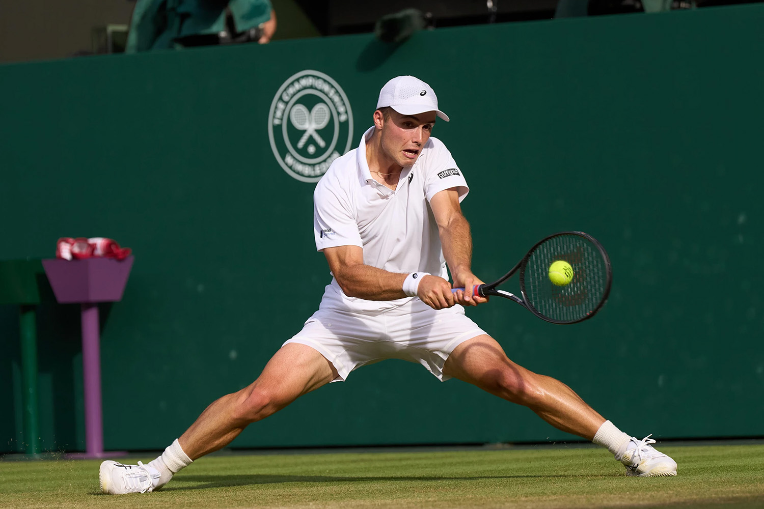 Arthur Fery lunges wide with a two-handed backhand to reach the ball on a grass court at Wimbledon.