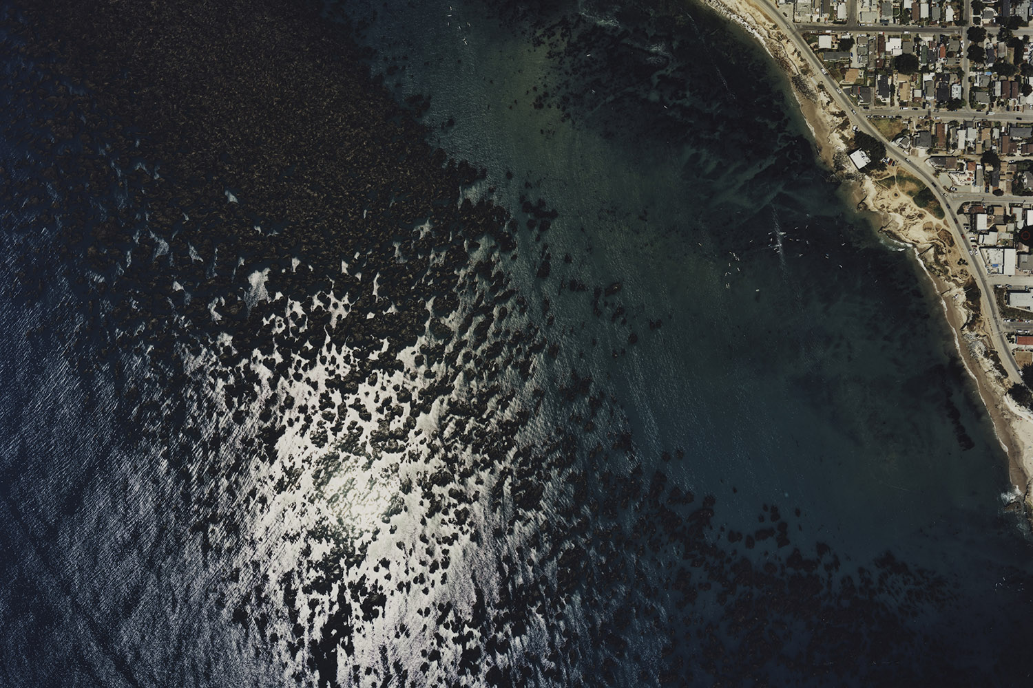 An aerial view of a coastline, showing the ocean, shoreline, and nearby residential areas.