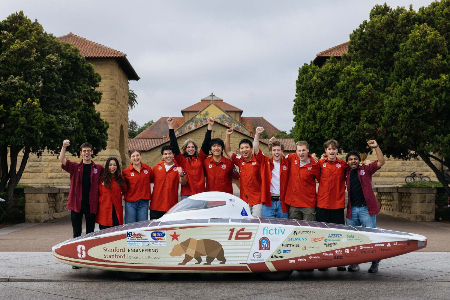Stanford's solar car team pose together for a photo behind their car, with Memorial Church in the background.