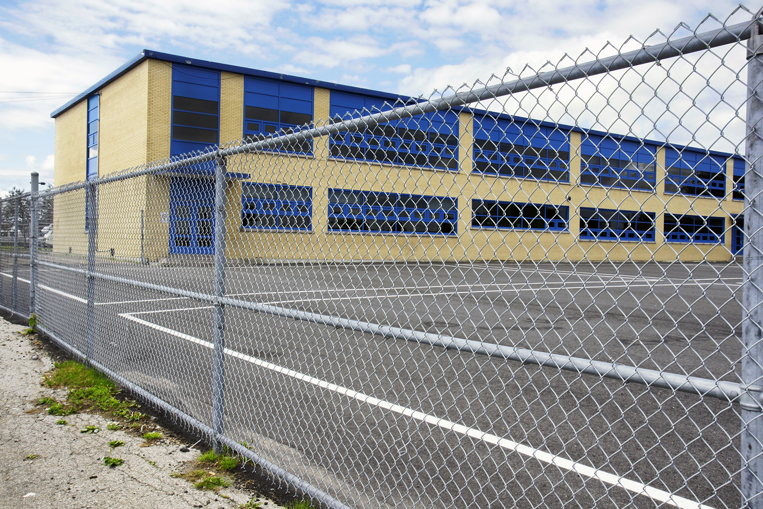 A school building with blue windows is seen behind a chain-link fence.