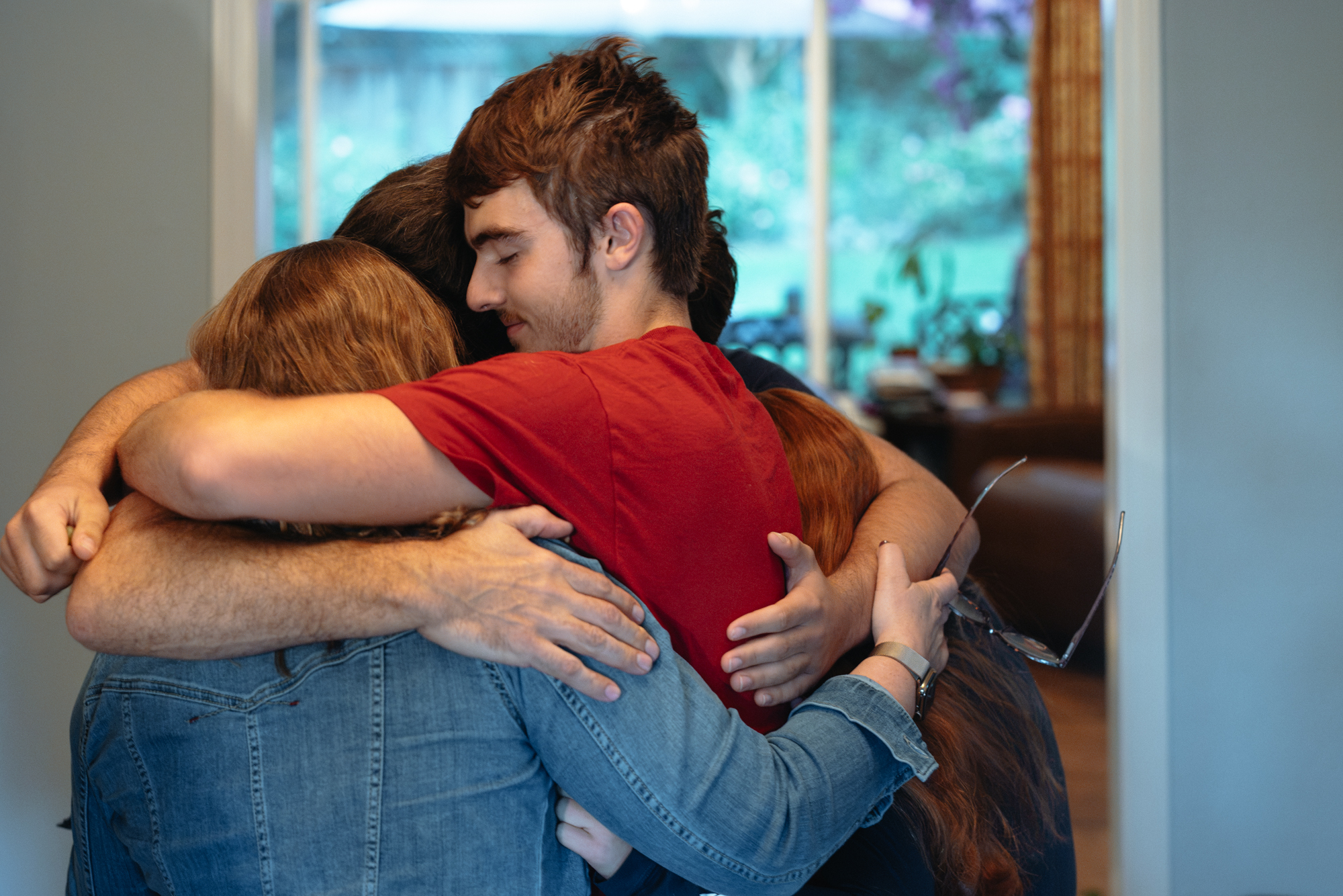 Alexander Deisseroth in a red T-shirt closes his eyes during a group hug at home.