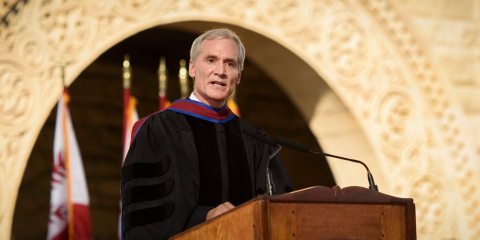 Marc Tessier-Lavigne at the podium with flags and arches in the Main Quad in the background.