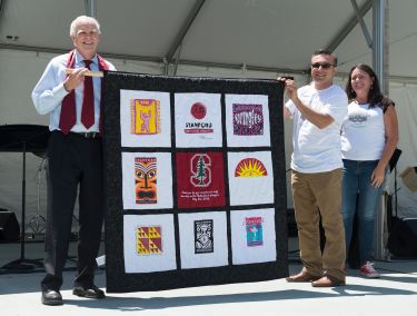 John Hennessy and Victor Madrigal holding a T-shirt quilt gift while Sheila Sanchez looks on