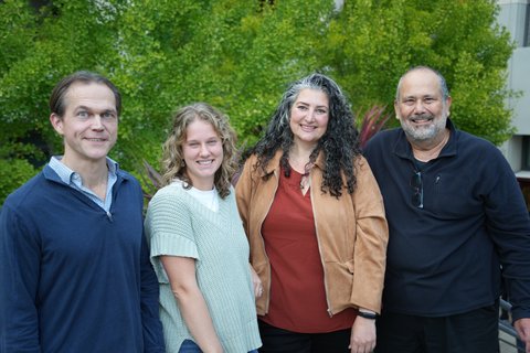 Group of four people stand and smile