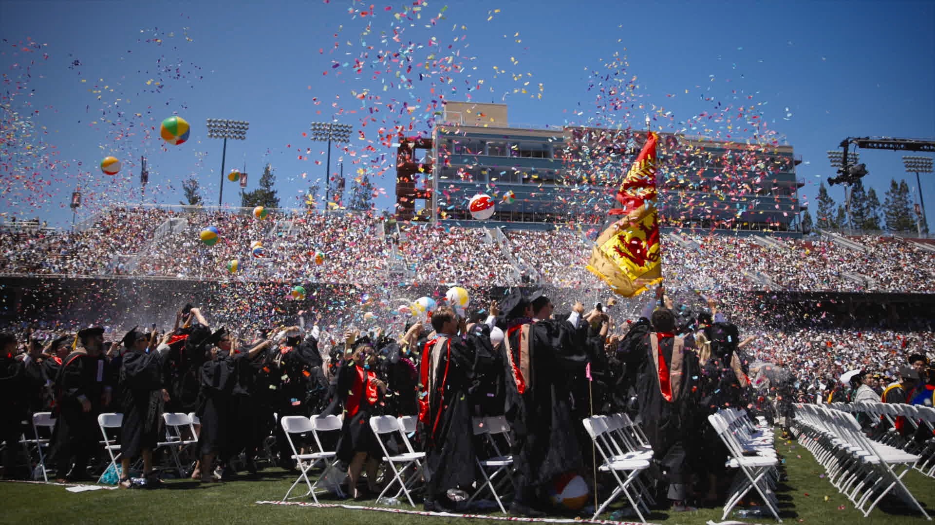 Graduates joyfully throw confetti on the field at Stanford stadium. (opens in a modal)
