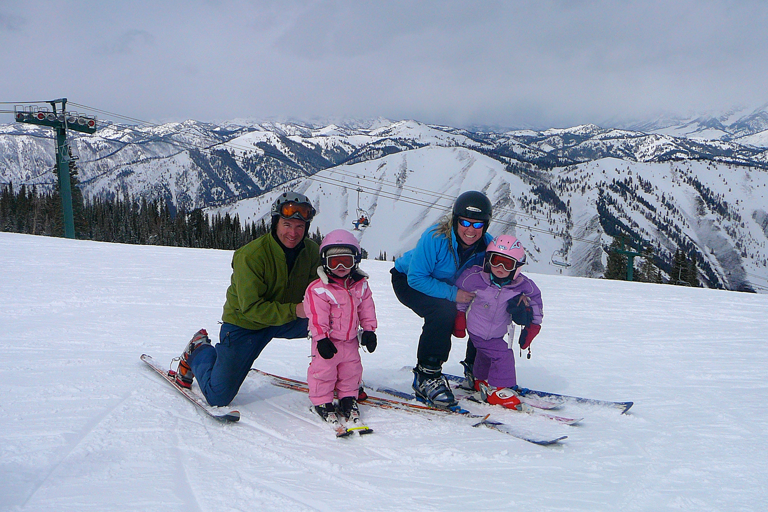 The Smith family is skiing on a snowy mountain, posing together with ski equipment and a scenic backdrop of mountains.