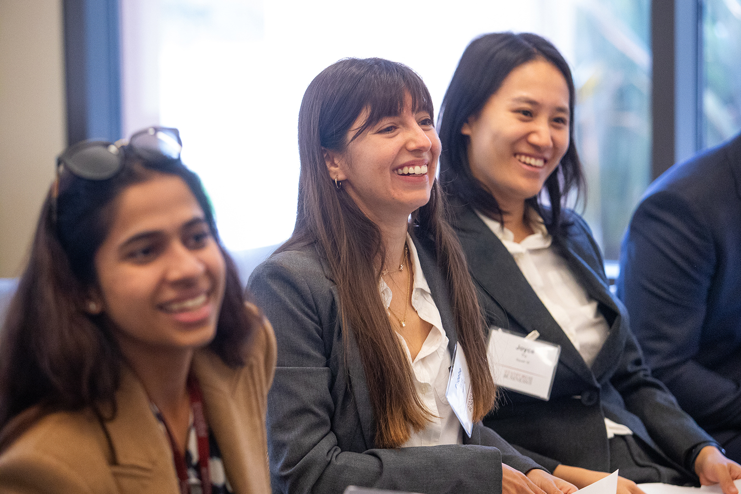 A group of individuals attentively listening during a presentation, dressed in professional attire, and seated indoors.