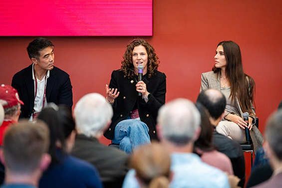 A panel discussion featuring speakers engaging an audience, against a red backdrop.