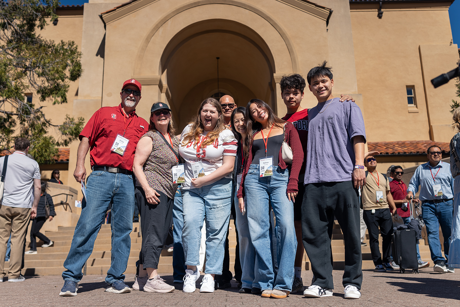 A group of people poses together in front of a large archway during Family Weekend, wearing name badges and holding brochures.