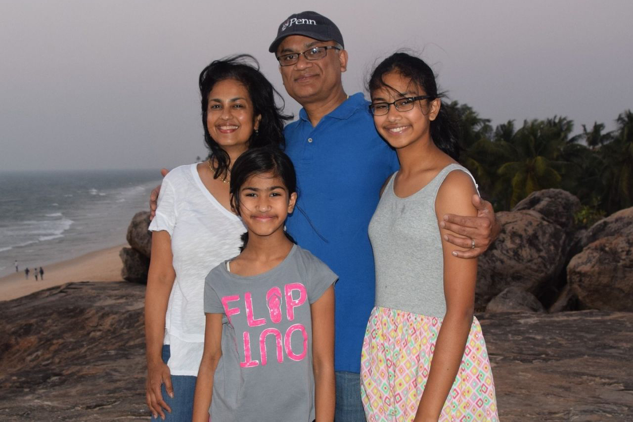 Seshadri family poses together smiling on a beachside rock formation.