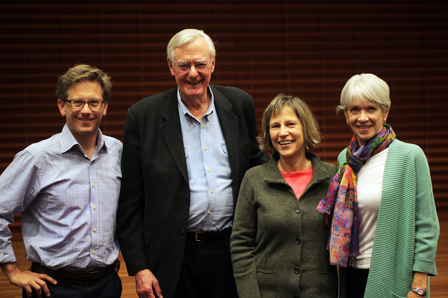 Rob Reich, Buzz McCoy, Debra Satz, and Barbara McCoy pose together in a group photo against a wooden backdrop.