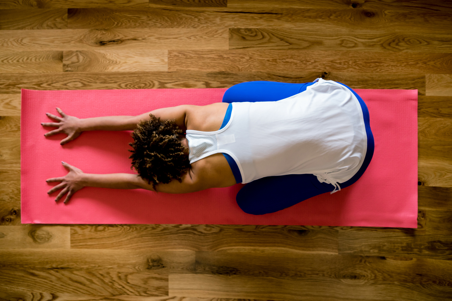 Overhead view of a woman in child pose on a pink yoga mat.