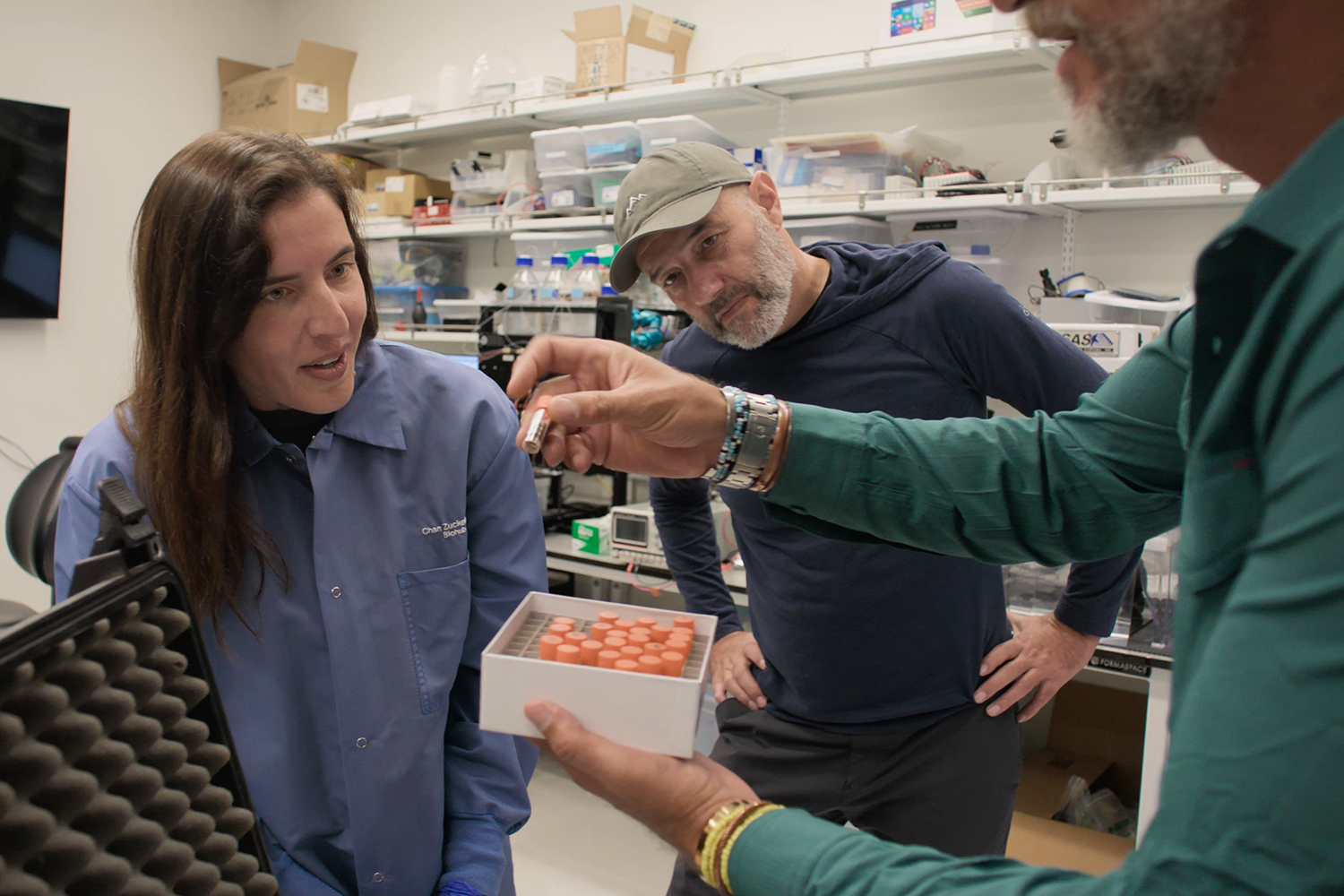 In a lab, people discuss a small container of samples.