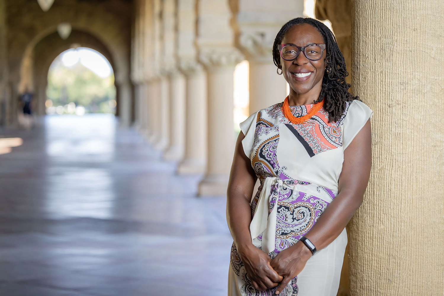 Rachel Jean-Baptiste in a patterned dress leans against a column in a Quad arcade.