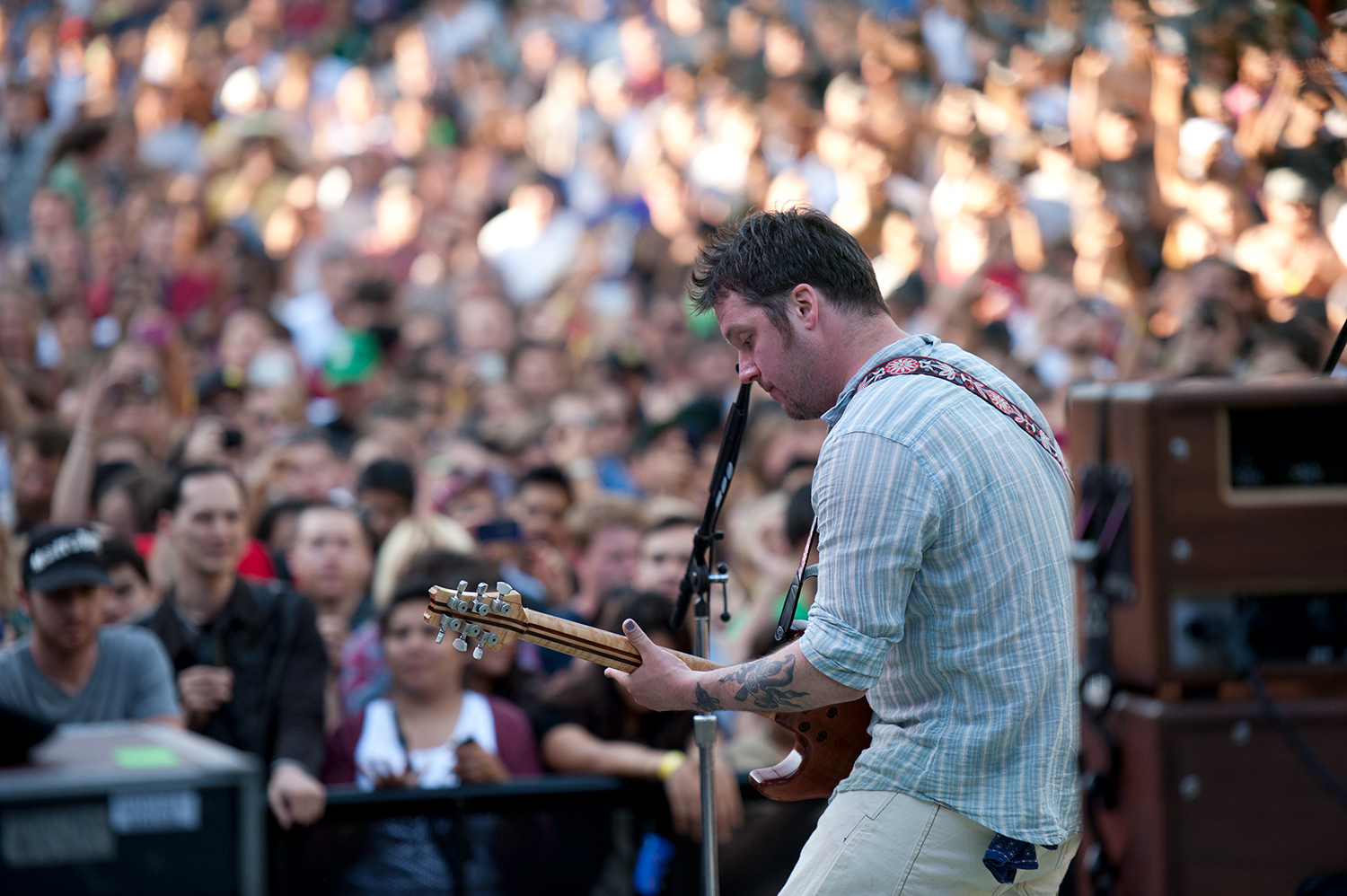 Modest Mouse playing guitar on stage in front of a cheering crowd at a lively outdoor event.