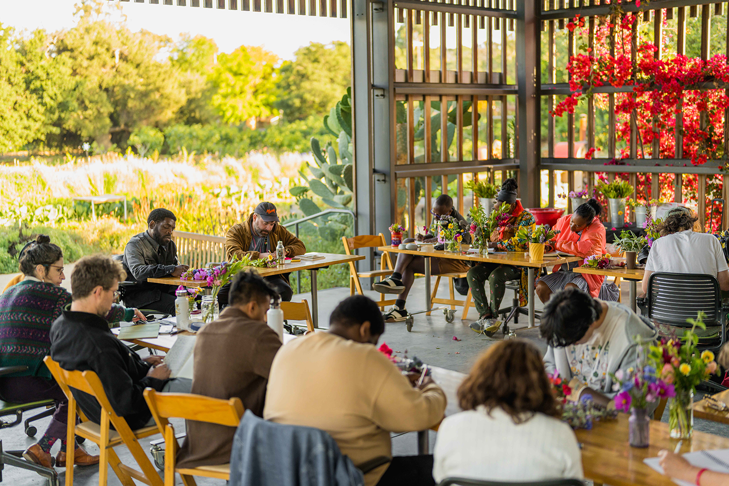Participants in a floral arrangement workshop gather indoors, creating arrangements surrounded by blooming plants and colorful decor.