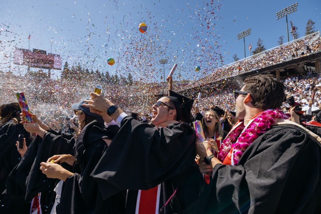 Open video Graduates celebrate with confetti and beach balls flying through the air at outdoor stadium ceremony. in a modal