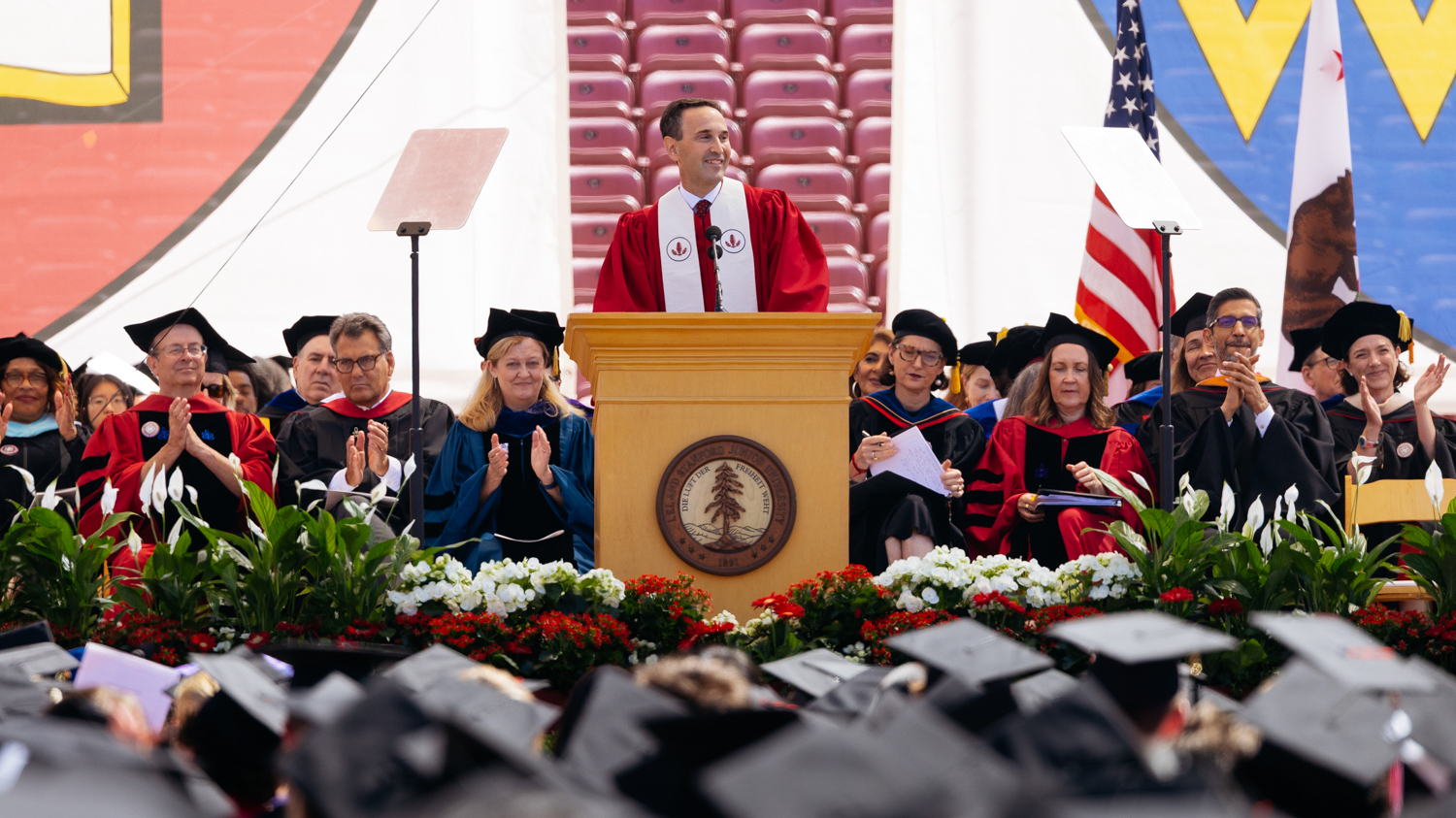 President Levin in red academic robes delivers his remarks at outdoor commencement ceremony.